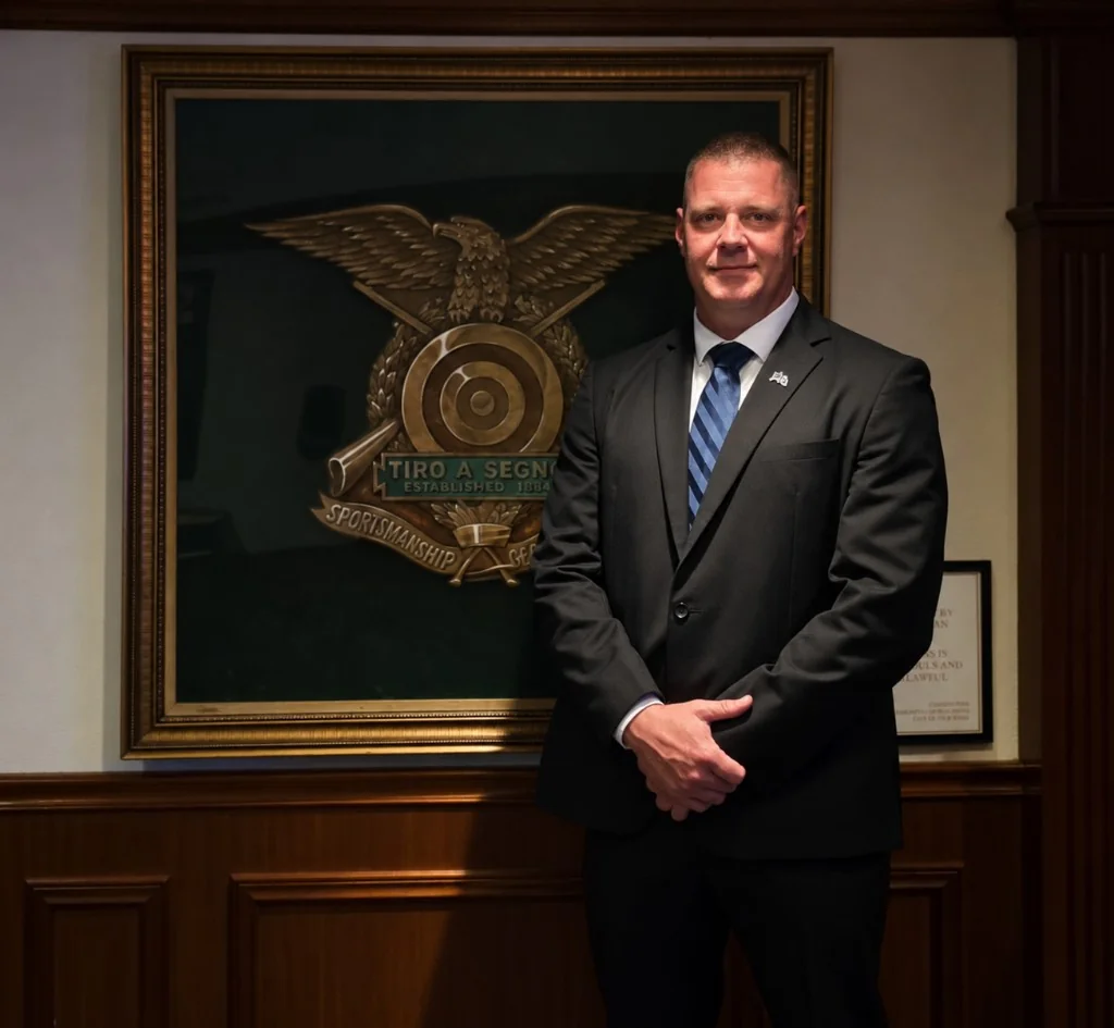 James Gonzales, owner of Shadow Securities LLC, in a dark suit standing beside the Tiro a Segno emblem in Greenwich Village, New York.