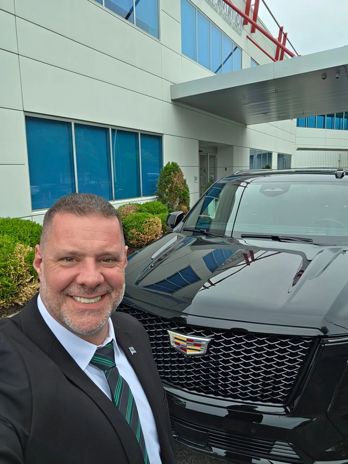 Shadow Securities protection agent in a suit beside a black Cadillac SUV staged at a private aviation FBO terminal entrance