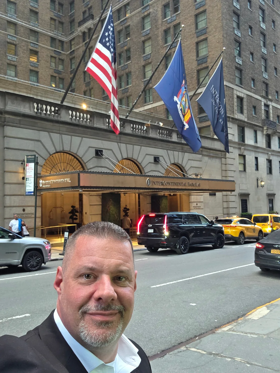 Shadow Securities protection agent outside a Midtown Manhattan hotel entrance with flags flying and a black SUV staged at the curb