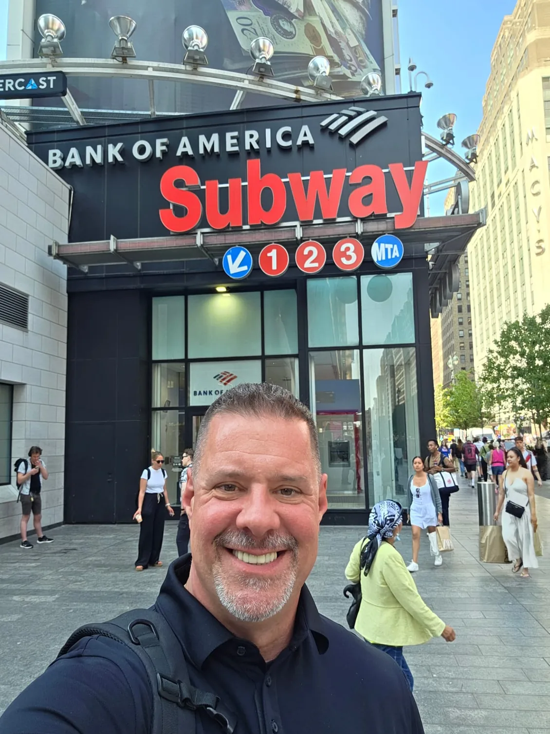 Shadow Securities protection agent beside a black SUV on a Midtown Manhattan street outside a Bank of America branch and subway entrance