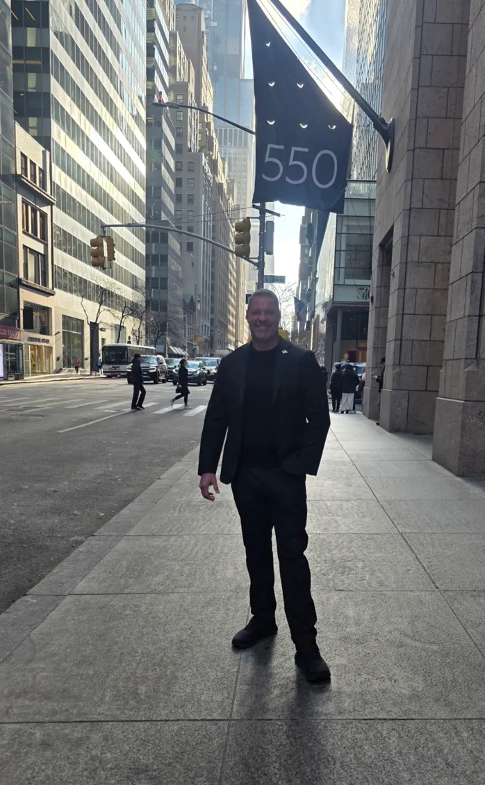 Protection agent standing on a Midtown Manhattan sidewalk beneath a 550 building flag